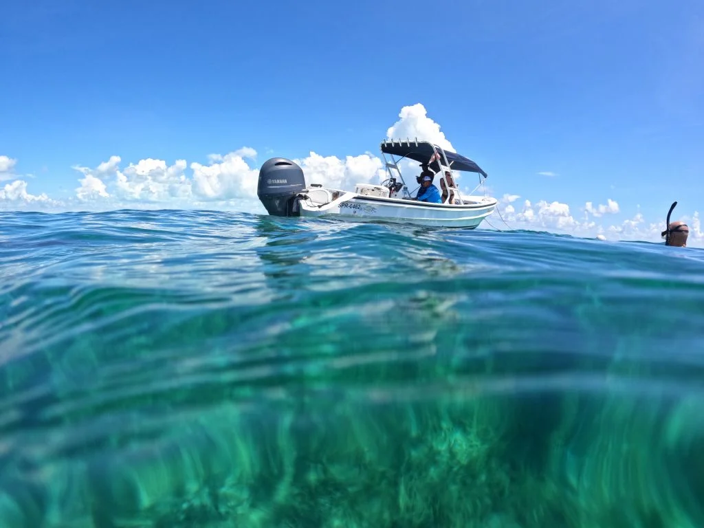 A boat floating above clear reef water in Belize